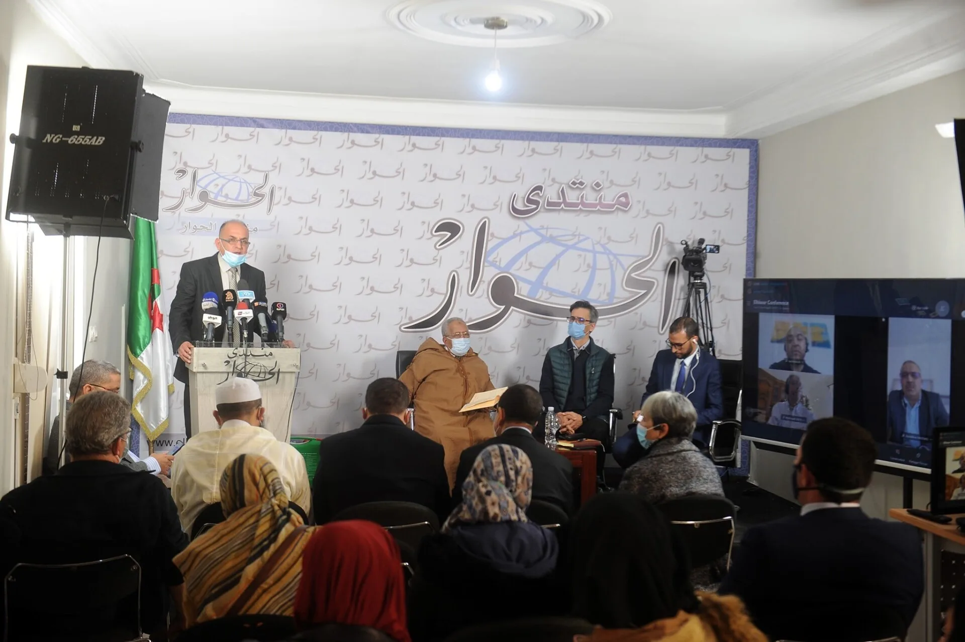 Conférence presse avec participants masqués et écran.